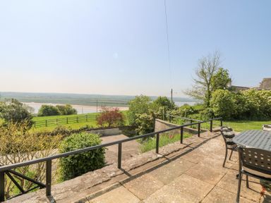 An outdoor patio area with a table and chairs overlooking a grassy field and a river beyond at Charlesworth in Braunton