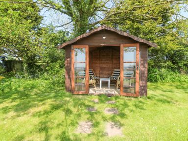 A wooden garden shed with glass doors two chairs and a small table inside on a lawn at Charlesworth in Braunton