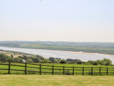 A green field with a wooden fence overlooking a river and distant hills at Charlesworth in Braunton