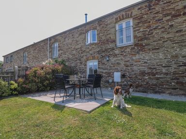 A stone building with a patio set and two dogs on grass at Sundowner in Padstow