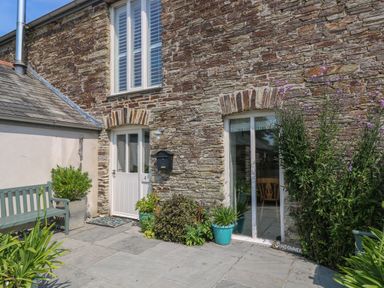 Stone house exterior with white door and window and potted plants on patio at Sundowner in Padstow