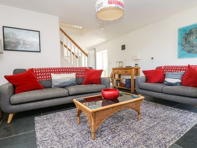 A living room with two gray sofas with red pillows a wicker coffee table and a wooden console table at Sundowner in Padstow
