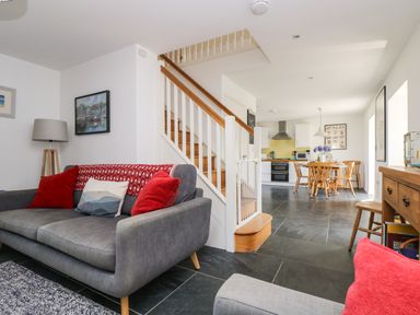 An open living and dining area with a gray sofa and red cushions near wooden stairs and a dining table with chairs at Sundowner in Padstow