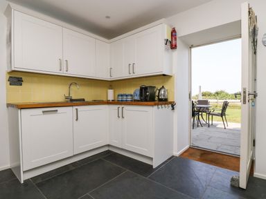 A kitchen with white cabinets a wooden countertop a sink coffee maker kettle and an open door leading to an outdoor patio at Sundowner in Padstow