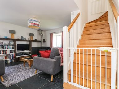 A living room with a gray sofa red cushions a TV bookshelf and wooden stairs with a safety gate at Sundowner in Padstow