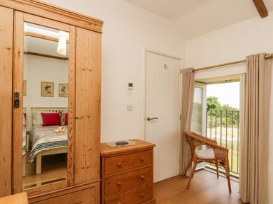A bedroom with wooden wardrobe and chest of drawers and a chair near an open window at Sundowner in Padstow