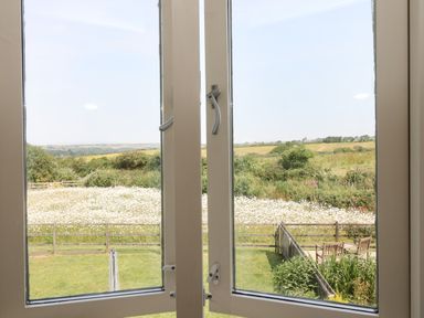 A view through a window of a garden with chairs and a table and fields beyond at Sundowner in Padstow