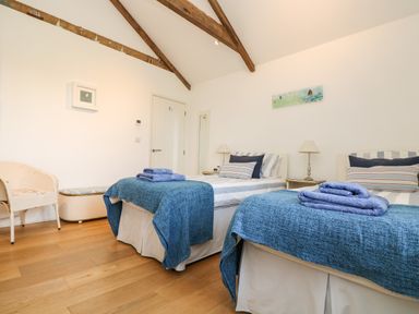 A bedroom with two single beds blue blankets and folded towels wooden floor and white walls at Sundowner in Padstow