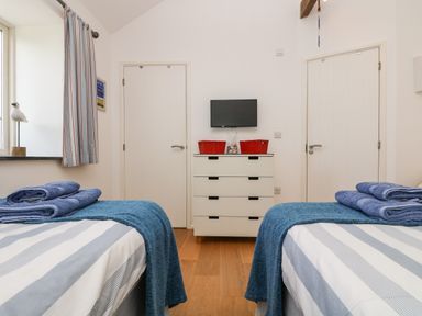 A bedroom with two single beds with blue towels and blankets a white chest of drawers and a wall-mounted TV at Sundowner in Padstow