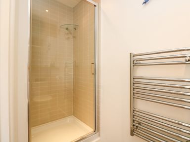A tiled shower enclosure with a glass door and a wall-mounted metal towel rack in a bathroom at Sundowner in Padstow