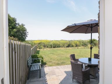 A patio area with a table umbrella and chairs next to a wooden bench and a grass lawn at Sundowner in Padstow