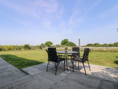 An outdoor patio with a metal table and four chairs on a stone surface overlooking a grass lawn and fenced garden at Sundowner in Padstow