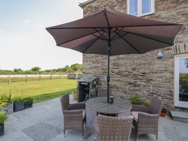An outdoor patio with a round table and four wicker chairs under a large umbrella near a stone wall at Sundowner in Padstow