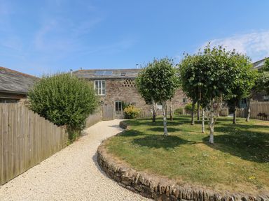 A gravel path leading to a stone building with a garden and trees at Sundowner in Padstow