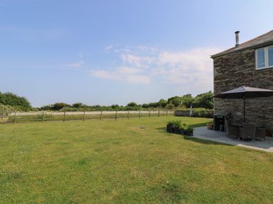 A garden with a lawn and patio furniture with an umbrella next to a stone house at Sundowner in Padstow