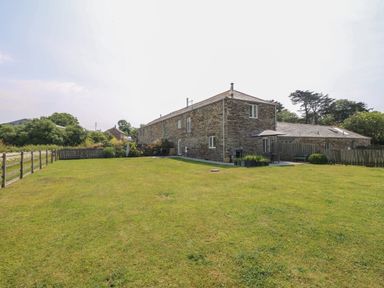 A large stone building with a fenced grassy yard and outdoor seating area at Sundowner in Padstow