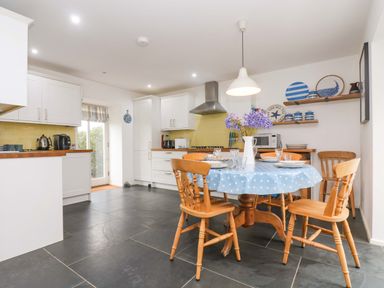 A kitchen with a round dining table covered with a blue polka dot tablecloth and wooden chairs at Sundowner in Padstow