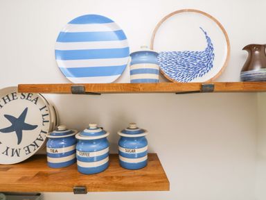 Blue and white striped canisters labeled tea coffee and sugar on a wooden shelf with matching plates and a jug at Sundowner in Padstow