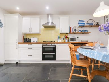 A kitchen with white cabinets wooden countertop and dining table with blue polka dot tablecloth at Sundowner in Padstow
