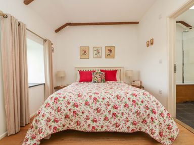 A bedroom with a bed covered in floral bedding and red pillows two lamps on bedside tables and a bathroom visible through an open door at Sundowner in Padstow