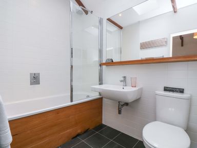 A bathroom with a bathtub with wooden paneling a glass shower screen a wall-mounted sink and a toilet at Sundowner in Padstow
