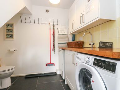 A utility room with washing machine sink ironing board broom and toilet at Sundowner in Padstow