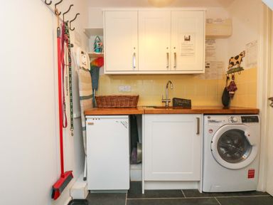 A laundry room with a washing machine, cabinets, countertop, broom, and cleaning supplies at Sundowner in Padstow