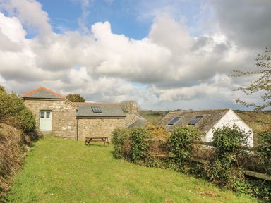 A grassy yard with bushes and a wooden picnic table near stone and white houses at Lower Rissick Cottage in Sennen