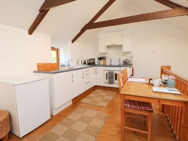 A kitchen with white cabinets wooden dining table with chairs and wooden beams on ceiling at Lower Rissick Cottage in Sennen