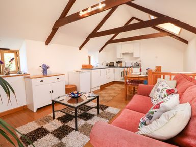 A living area with a red sofa, glass coffee table, white cabinets, dining table, and kitchen appliances at Lower Rissick Cottage in Sennen