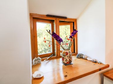 A wooden windowsill with a floral vase of purple and orange flowers and various stones and shells at Lower Rissick Cottage in Sennen