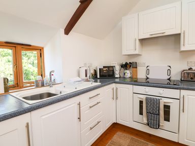 A kitchen with white cabinets a sink a microwave a kettle and an oven at Lower Rissick Cottage in Sennen