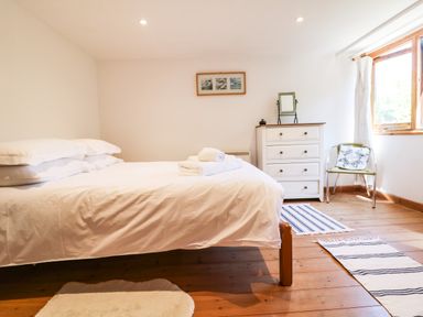 A bedroom with a bed with white linens a white chest of drawers a chair and rugs on wooden floor at Lower Rissick Cottage in Sennen