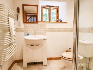 A bathroom with a sink, toilet, window, mirror, and a towel radiator at Lower Rissick Cottage in Sennen