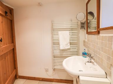 A bathroom with a wooden door radiator with towel wall mirror and a sink with soap dispenser at Lower Rissick Cottage in Sennen
