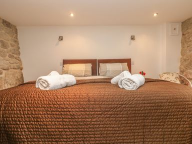 A bedroom with a bed covered with a brown quilt and towels on top at The Old Barn in Sennen