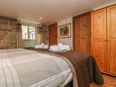 A bedroom with a bed with folded towels wooden wardrobes a wooden door a window with curtains and a framed picture on the wall at The Old Barn in Sennen