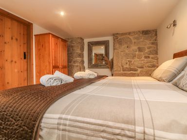 A bedroom with a bed with folded towels on a brown blanket a wooden wardrobe a wooden door a mirror and stone walls at The Old Barn in Sennen