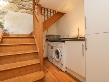 A laundry area with a washing machine and dryer under a wooden staircase at The Old Barn in Sennen
