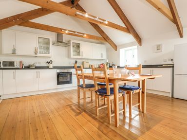 A kitchen with wooden dining table and chairs under wooden ceiling beams at The Old Barn in Sennen