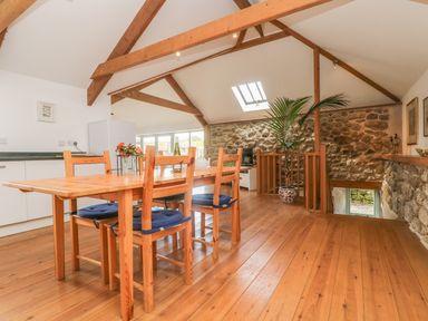 A dining area with a wooden table and chairs and exposed stone walls at The Old Barn in Sennen