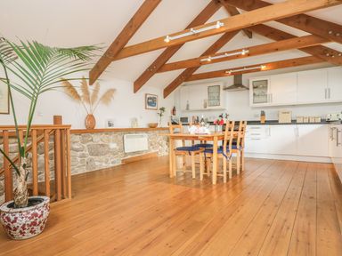 A kitchen and dining area with wooden beams a wooden table with chairs and a potted plant at The Old Barn in Sennen