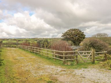 A gravel and grass path with wooden fences and a gate in a rural area with trees and fields at The Old Barn in Sennen