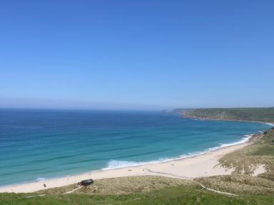 A sandy beach with people near the shore and grassy hills by the sea at The Old Barn in Sennen