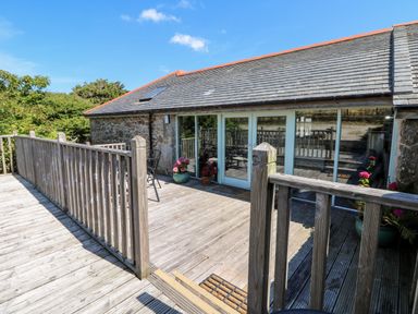 A wooden deck with railing and potted plants outside a stone building with glass doors at The Old Barn in Sennen