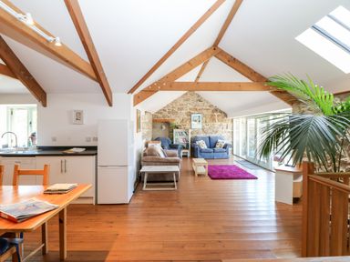 An open living space with wooden beams a kitchen area wooden floor and seating at The Old Barn in Sennen