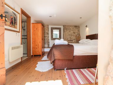 A bedroom with a double bed a wooden wardrobe a wall mirror and a bathroom visible through a door at The Old Barn in Sennen