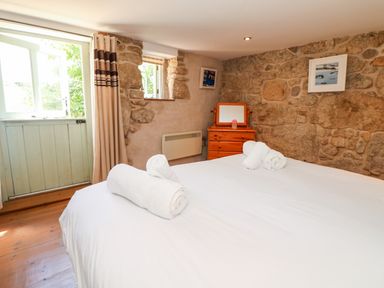 A bedroom with a bed covered in white linens and rolled towels a wooden dresser and stone walls at The Old Barn in Sennen