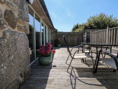 An outdoor wooden deck with a glass table and four chairs and two flower pots at The Old Barn in Sennen