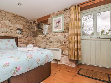 A bedroom with stone walls a bed with floral bedding and a door with a curtain at Barneys Barn in Sennen